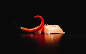 Кусок красной рыбы с острым красным перцем на черном фоне