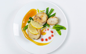 Кусочки жареной рыбы на белой тарелке с лимоном и зеленью