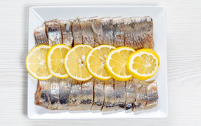 Селедка нарезанная кусочками на белой тарелке с лимоном 