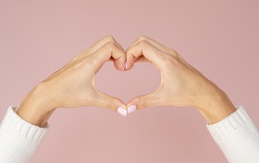 Девушка делает сердце руками на розовом фоне 