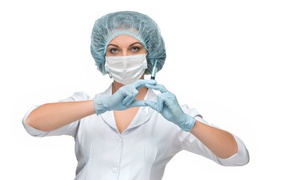 Девушка медсестра в маске со шприцем в руках на белом фоне