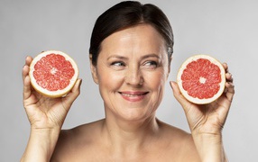 Улыбающаяся женщина с грепфрутом в руках на сером фоне
