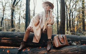 Девушка в пальто сидит на упавшем дереве в лесу 