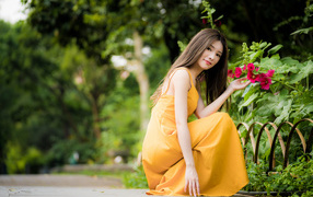 Девушка в желтом платье сидит у цветка мальвы в парке