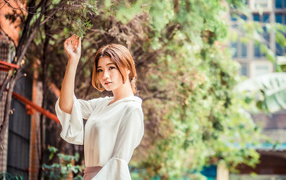Молодая азиатка в белой блузке стоит у дерева 