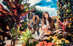 Молодая азиатка сидит возле клумбы с цветами