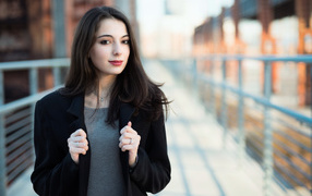 Молодая девушка в черном пальто стоит на мосту