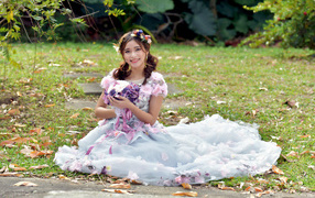 Девушка азиатка в красивом платье сидит на земле с букетом 