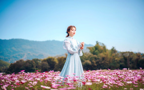 Девушка азиатка в красивом платье идет по полю с цветами космеи