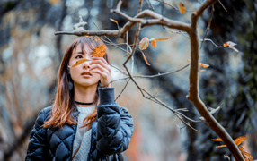 Asian girl in a black jacket near a tree