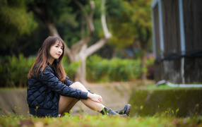 Девушка азиатка в черной куртке сидит на траве