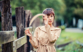 Девушка азиатка в пальто стоит у забора 