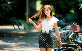 Девушка азиатка в юбке в горох у велосипеда трогает волосы