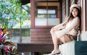 Девушка азиатка в свитере сидит на пороге 