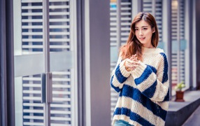 Девушка азиатка в теплом свитере стоит у окна