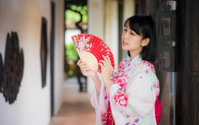 Девушка азиатка в кимоно с веером в руке стоит у ворот 