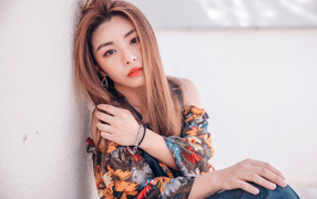 Девушка азиатка сидит на полу у стены 