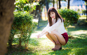 Девушка азиатка сидит на корточках в парке