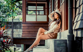 Девушка азиатка с закрытыми глазами сидит на ступеньках дома 