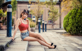 Азиатка в шортах сидит на ступенях 