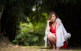 Азиатка в красном платье сидит в парке 
