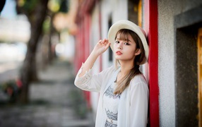 Красивая азиатка в шляпе стоит у стены