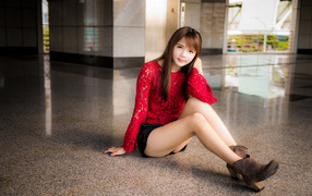 Красивая девушка азиатка в красной блузке сидит на полу