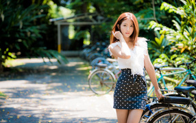 Красивая девушка азиатка в юбке в горох стоит у велосипеда 