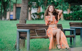 Красивая девушка азиатка в костюме сидит на лавке