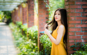 Beautiful Asian girl in a yellow dress is standing by a brick column.