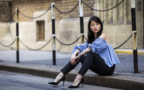 Красивая девушка азиатка в черных брюках сидит на земле