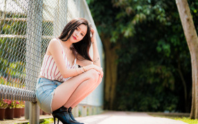 Красивая девушка азиатка сидит у железной сетки