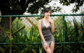 Красивая азиатка в сером платье стоит у зеленой сетки 