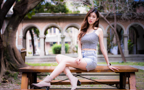 Красивая азиатка сидит на лавочке в парке