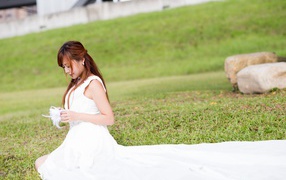 Красивая девушка азиатка в свадебном платье сидит на траве