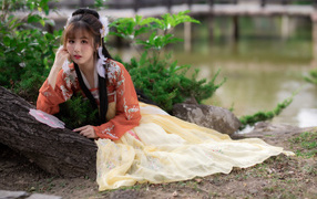 Красивая девушка азиатка сидит на земле у дерева 