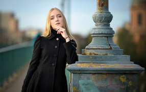 Красивая блондинка в черном пальто стоит у фонаря