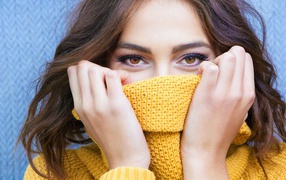 Красивая кареглазая девушка закрывает лицо свитером