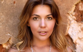 Красивая кареглазая девушка стоит у стены 