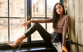 Красивая брюнетка в черных брюках сидит на окне 