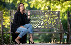 Beautiful girl in a black coat sits on a bench in the park