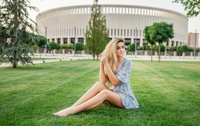 Красивая девушка в платье сидит на зеленом газоне 