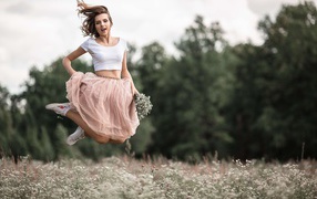 Красивая девушка в юбке прыгает на поле с ромашками