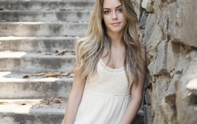 Красивая девушка в белом платье у каменной стены 