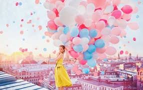 Красивая девушка в желтом платье стоит на крыше с воздушными шариками