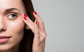 Красивая девушка модель мажет лицо кремом на сером фоне 