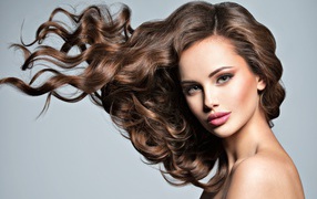 Красивая девушка модель с волнистыми волосами на сером фоне