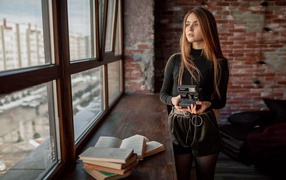 Красивая девушка с фотоаппаратом в руках у окна 