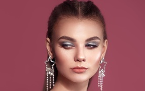 Красивая девушка с макияжем и большими серьгами на розовом фоне