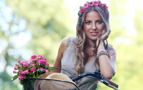 Beautiful girl with roses on a bicycle with a wreath on her head